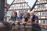 Zwei Männer und zwei Frauen in Wanderkleidung stehen an einem Brunnen in der Stadt Gudensberg.