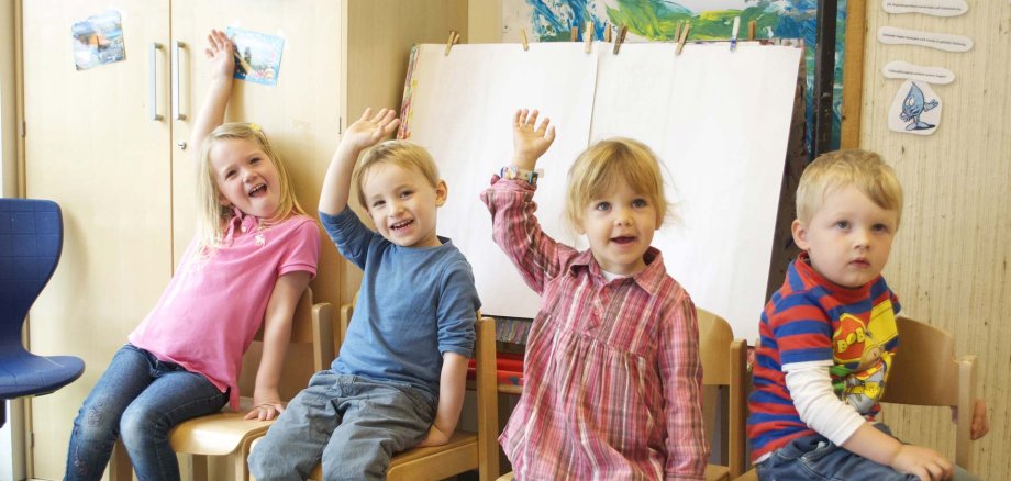 Sitzende Kinder heben die Hände