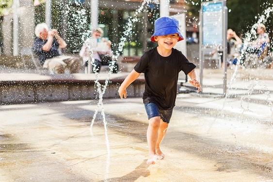 Little boy running between water jets in fountain
