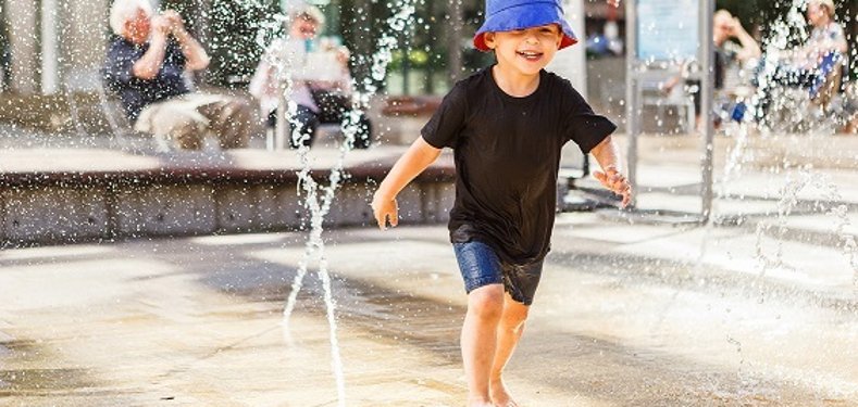 Little boy running between water jets in fountain
