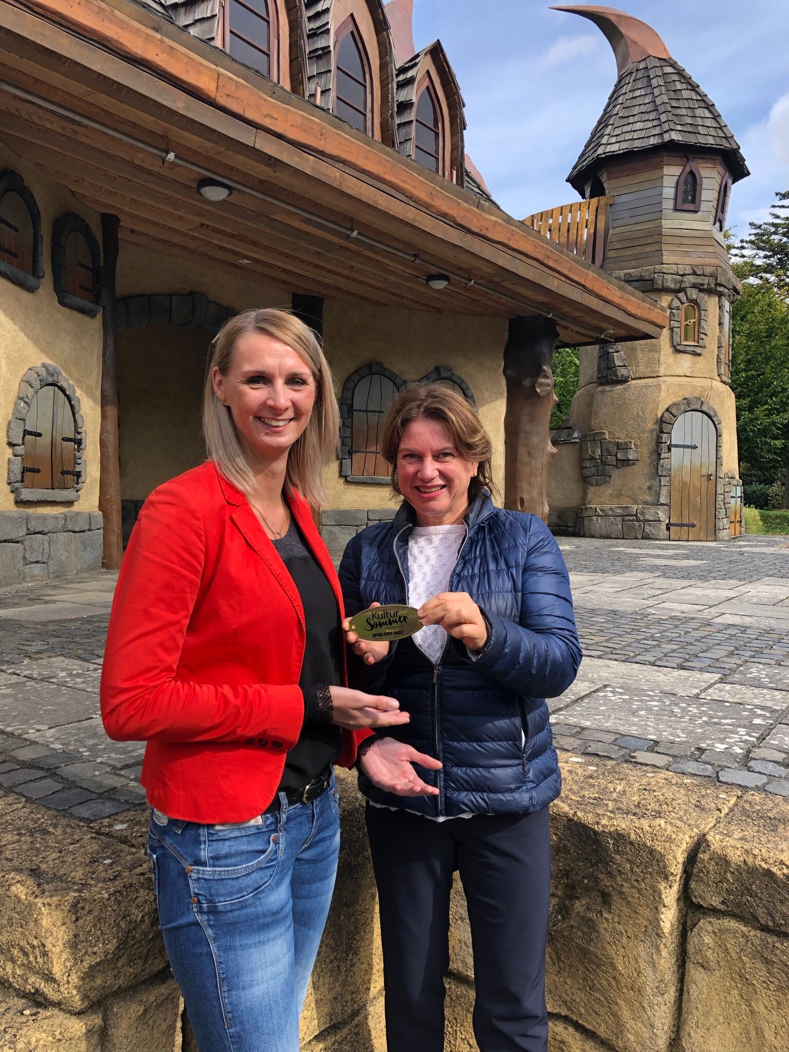 Bürgermeisterin Sina Best (links) bekommt von Frau Matthes (Geschäftsführerin vom Kultursommer Nordhessen) die goldene Plakette „Spielort 2022“ für die Gudensberger Märchenbühne überreicht.