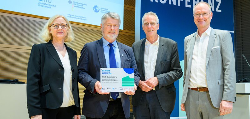 eine Frau und zwei Männer. Der Mann in der Mitte nimmt den Preis entgegen.