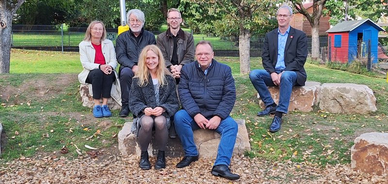 Sechs Gäste bei der Einweihung sitzen auf Steinen