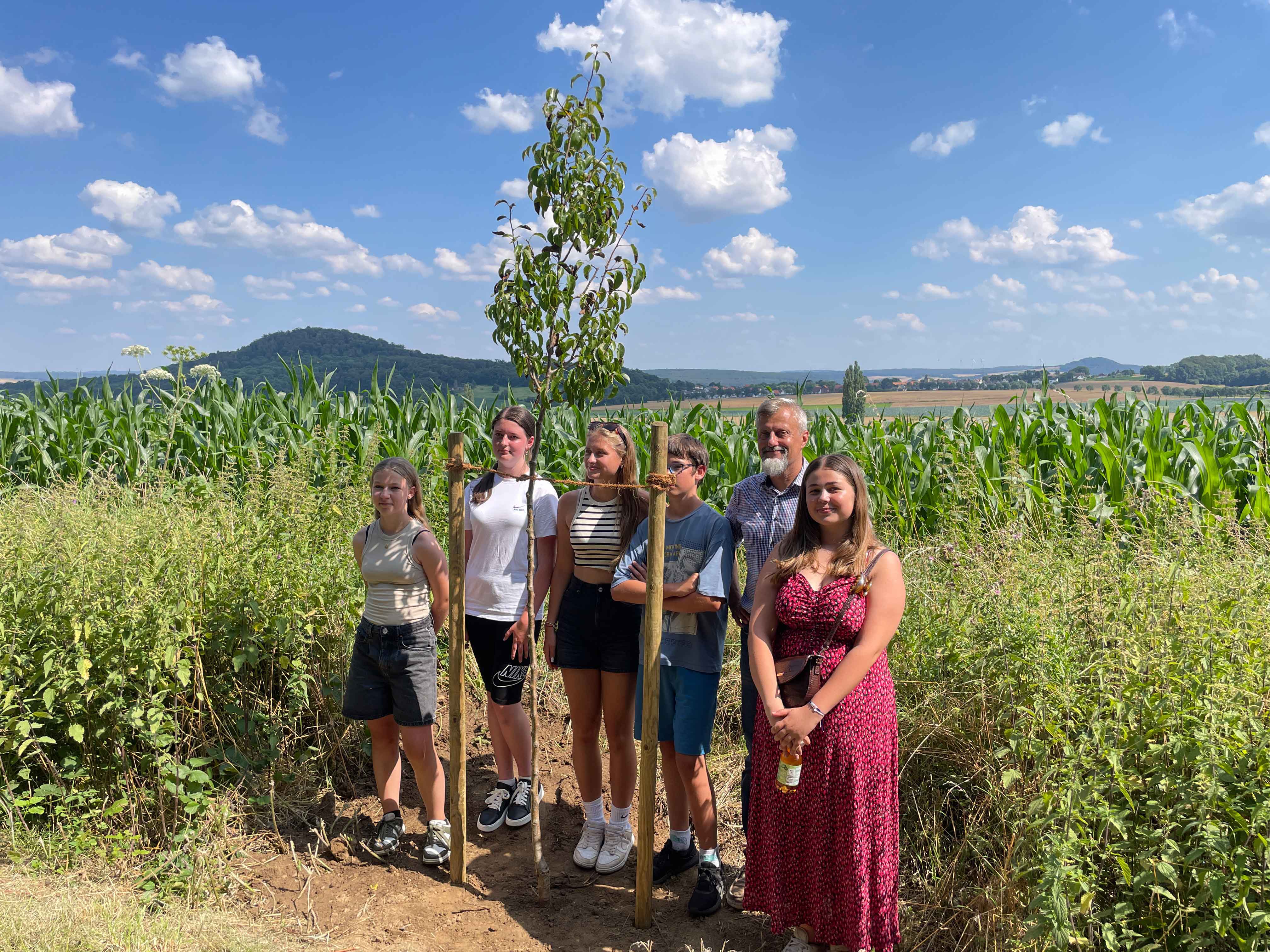 Jugendliche und Betreuer vor einem frisch gepflanzten Baum.