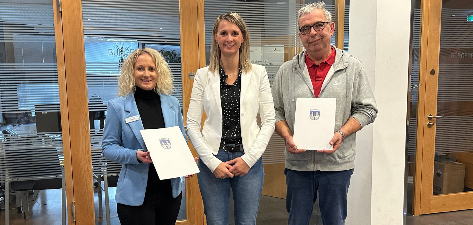 Bürgermeisterin und eine Kollegin und ein Kollege im Rathausfoyer mit Urkunden in der Hand