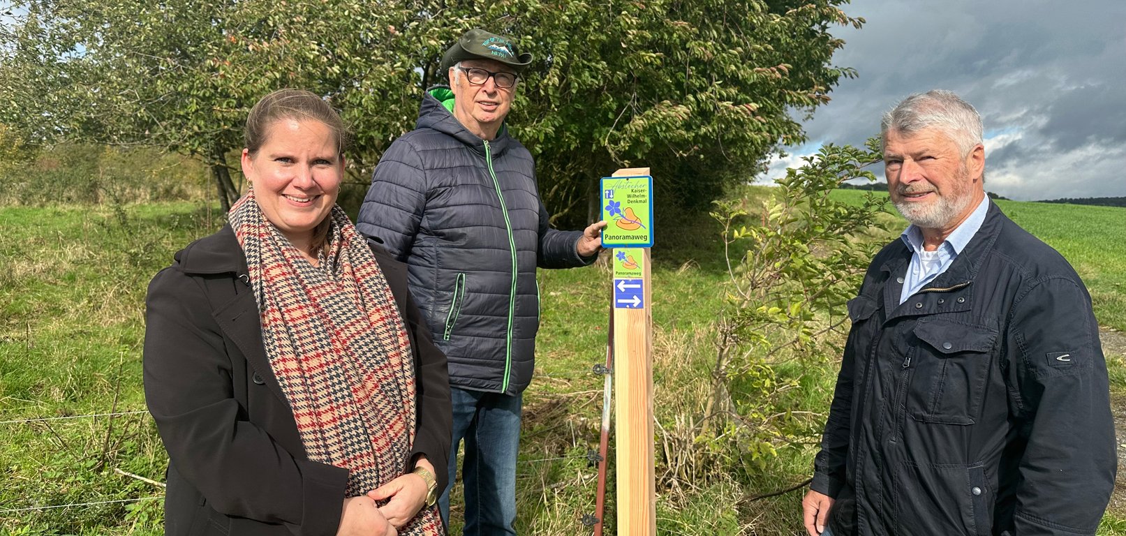 Zwei Männer und eine Frau mit einem Schild neben dem Panoramaweg