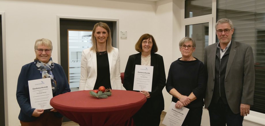 vier Frauen und ein Mann mit Urkunden in der Hand an einem Tisch stehend